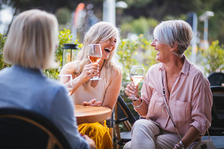 three friends sitting outside enjoying stories, laughs and some wine