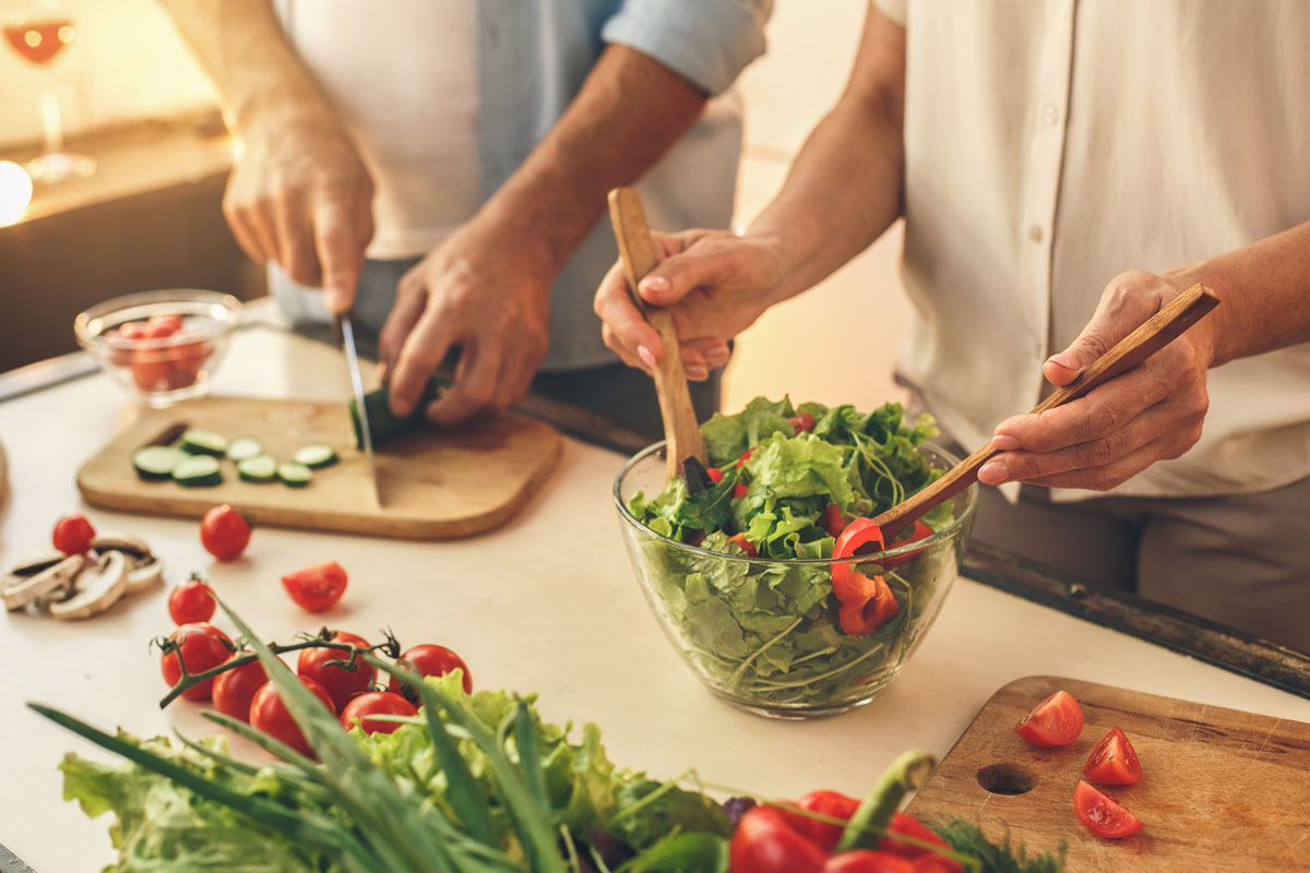 An elderly couple preparing a salad with tomatoes and cucumbers