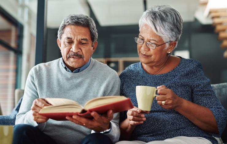An elderly couple sit on a couch and read a book together