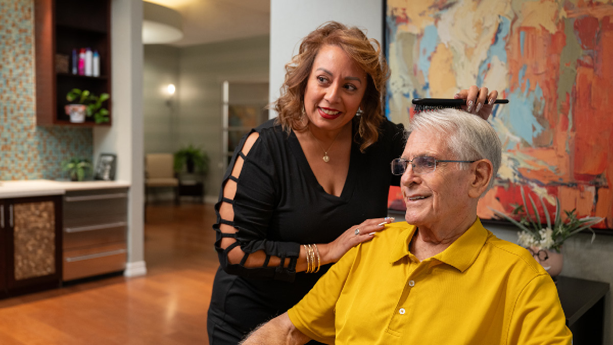 A hair stylist brushes a senior man's hair