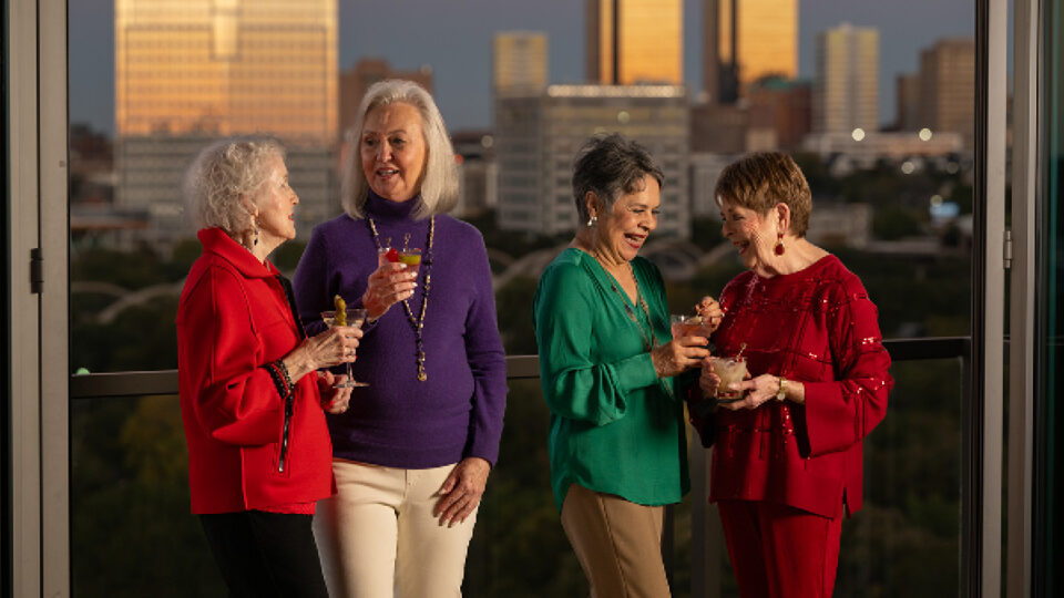 Four senior women enjoy a skyrise balcony with happy hour drinks