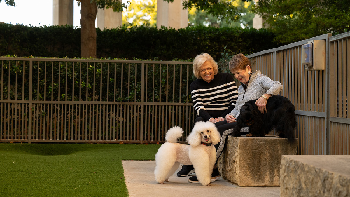 Two senior woman play with two dogs at the dog park at The Stayton