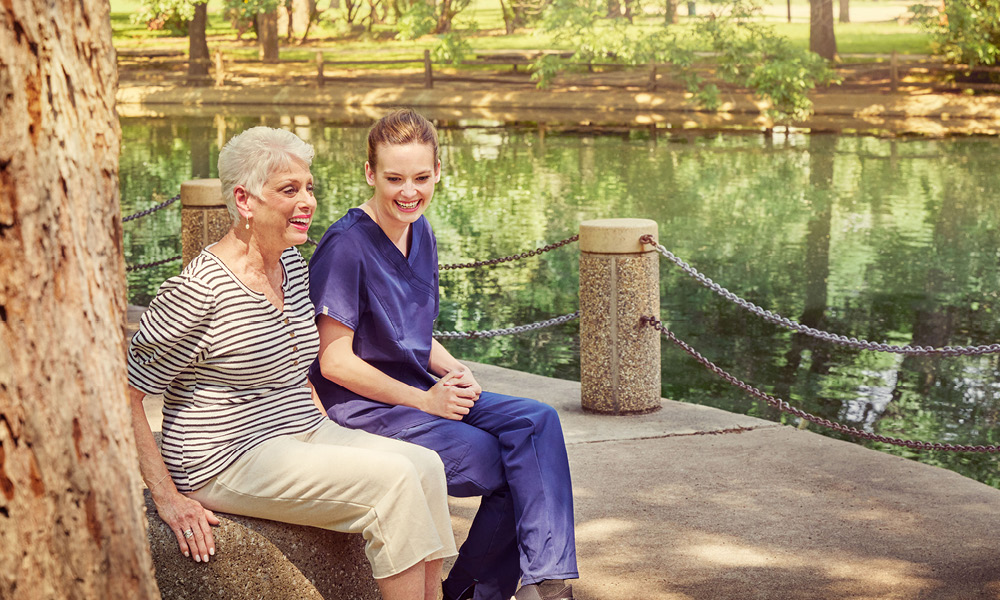 elderly lady smiling with her nurse while sitting by the creek.