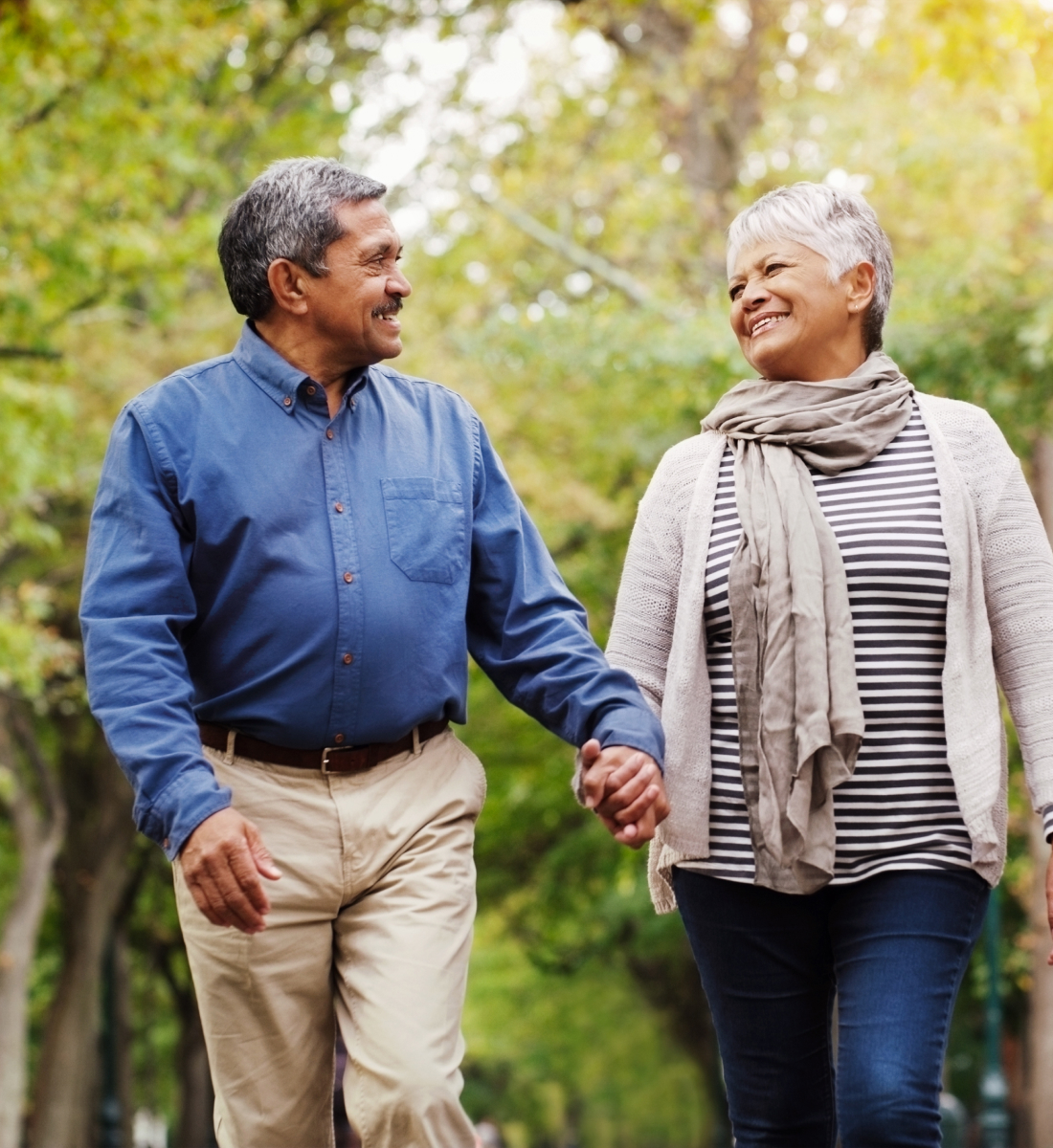 A senior man and a senior woman walk hand in hand in nature