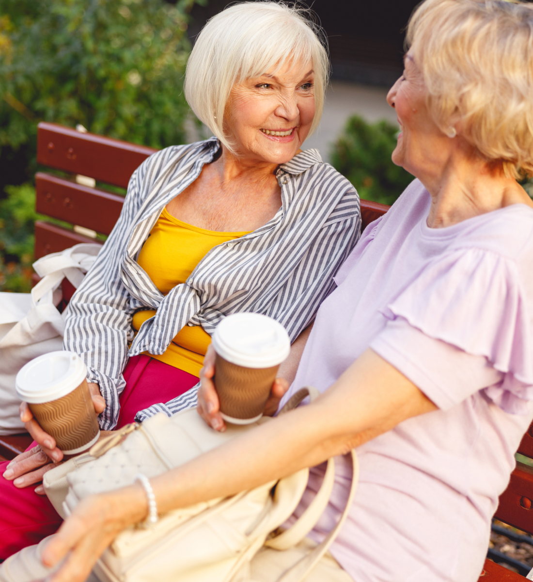 Two older women sit on a park bench while enjoying coffee to go
