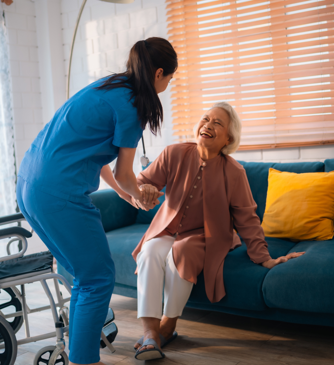A health care worked helps an older woman move from a couch to her wheelchair
