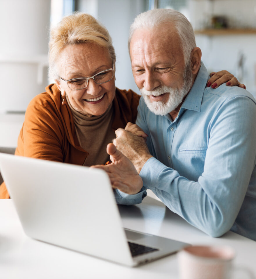 A senior woman and a senior man look at a laptop together