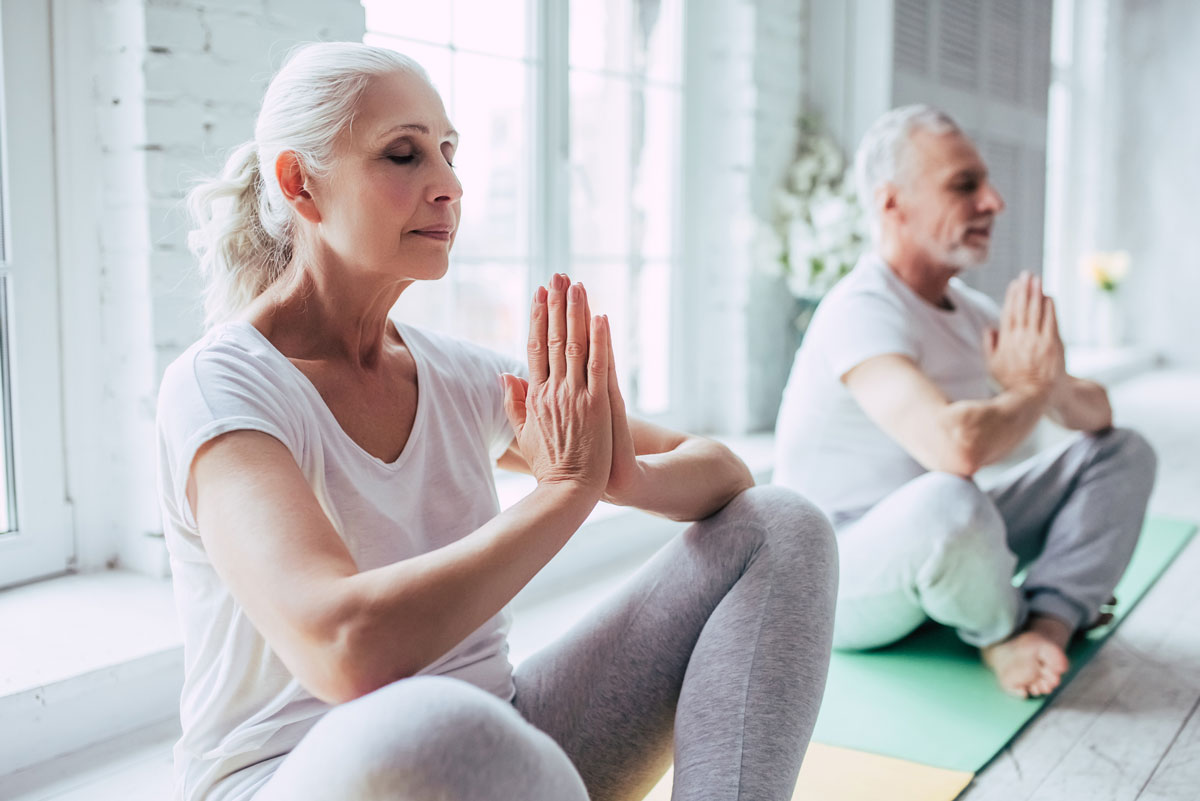 A senior man and woman sitting in a yoga pose