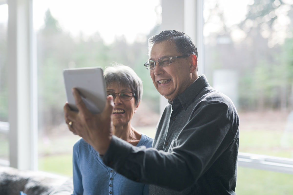 an elderly couple smiling while talking to someone over video chat on a tablet