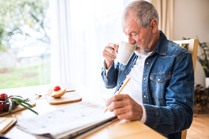 a senior man drinking a cup of coffee while reading the newspaper